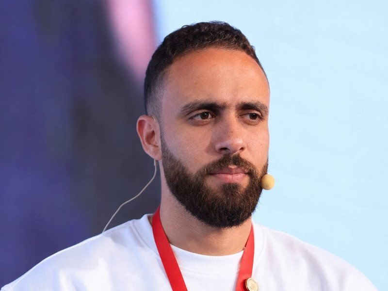 Portrait of Mohamed Arfaoui wearing a headset microphone and a white sweatshirt at a conference