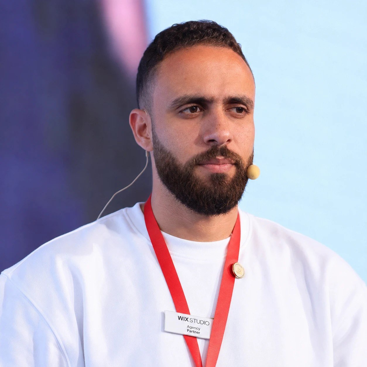 Portrait of Mohamed Arfaoui wearing a headset microphone and a white sweatshirt at a conference